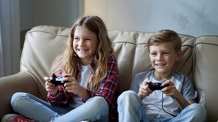 Two children play video games on beige sofa in candid photo; girl in plaid, boy in gray shirt.
