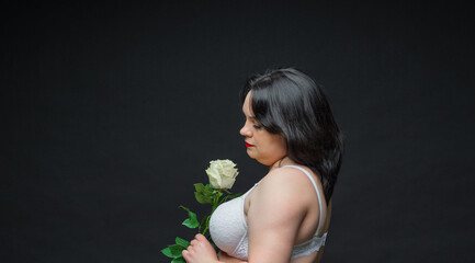 Beautiful woman in lingerie with a rose in her hands posing in a dark studio. She is wearing a white bra and black tights.