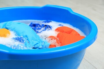 Basin with colorful clothes on floor, closeup. Hand washing laundry