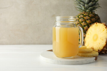 Tasty pineapple juice in mason jar and fresh fruits on white wooden table against grey background, closeup. Space for text