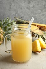 Tasty pineapple juice in mason jar and fresh fruits on grey textured table, closeup
