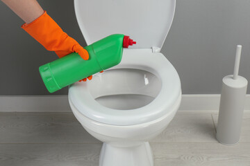 Woman cleaning toilet with detergent in bathroom, closeup