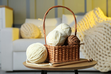 Wicker basket with colorful yarns and knitting needles on coffee table in cozy room