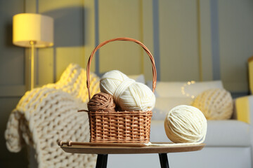 Wicker basket with colorful yarns and knitting needles on coffee table in cozy room