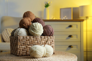 Wicker basket with colorful yarns and knitting needles on coffee table in cozy room