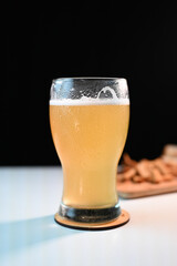glass of beer on a light table in a pub with a snack on a dark background