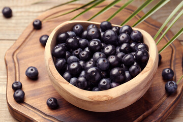 Ripe acai berries in bowl and palm leaves on wooden table, closeup