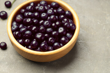 Ripe acai berries in bowl on grey textured table, closeup