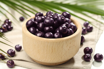 Ripe acai berries in bowl on light table, closeup