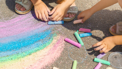 Kids paint outdoors. little girls drawing a rainbow colored chalk on the asphalt on summer sunny...