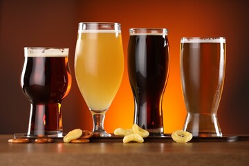 Glasses with different types of beer on wooden table against color background
