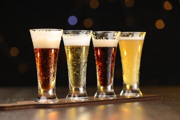 Glasses with different types of beer on wooden table against blurred lights, closeup