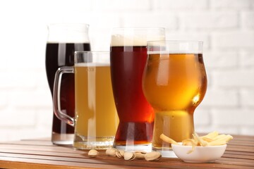 Glasses with different types of beer and snacks on wooden table against white wall, closeup