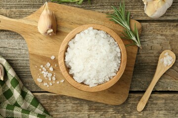 Sea salt in bowl, rosemary and garlic on wooden table, top view