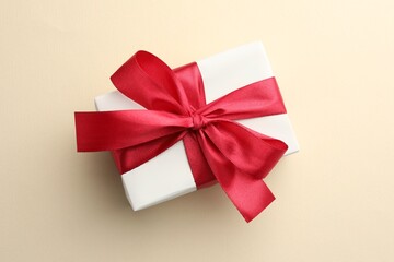 Beautiful gift box with red bow on beige background, top view