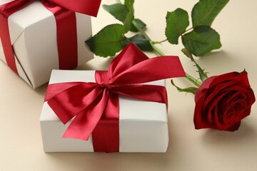 Beautiful gift boxes with red bows and rose on beige background, closeup