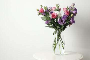 Vase with beautiful eustoma flowers on white table, space for text