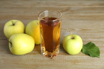 Glass of juice and apples on wooden table
