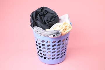 Plastic basket full of laundry on pink background