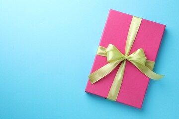 Gift box with bow on light blue background, top view. Space for text