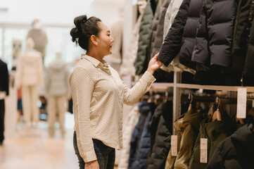 Woman browses through rows of jackets in stylish clothing store, contemplating her next fashion...