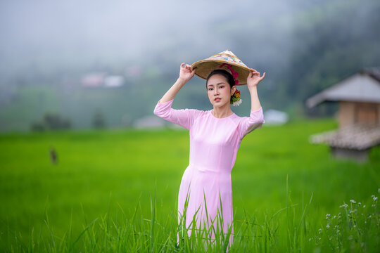 Beautiful women standing in a lush green tea field, likely in a rural area. They are wearing traditional conical hats and light-colored clothing with green tea platation background	