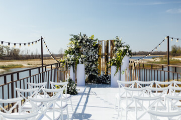 A wedding arch, decorated with flowers, stands on a podium, stands in the open air