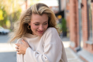 Close-up portrait of beautiful long haired caucasian blond woman in white sweater standing outdoor on city street in a sunny autumn morning. Soft focus. Beautiful people and fashion theme.