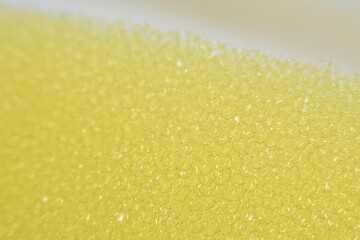 the texture and details of a kitchen sponge used for dishwashing. The sponge&rsquo;s porous surface is clearly visible, showcasing its small, irregular holes and soft
