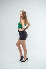 Fototapeta premium Woman in green top and black skirt posing in front of camera. She has long hair, she is standing on white background. Beautiful sexy body. Fitness and healthy eating concept.