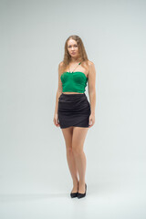 Fototapeta premium Girl in green top and black skirt poses for camera. She is wearing black heels and necklace. Beautiful sexy body.