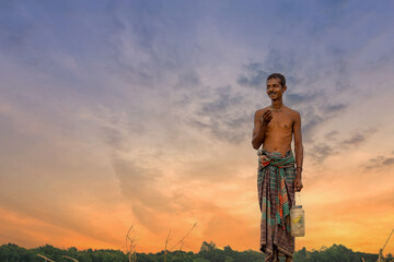 Riverside people of Bangladesh. A fisherman stands in the twilight horizon behind the river bank.