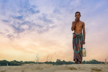 Riverside people of Bangladesh. A fisherman stands in the twilight horizon behind the river bank.