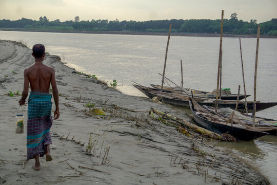 Riverside people of Bangladesh. A fisherman is walking along the river bank. The river flows along the side.