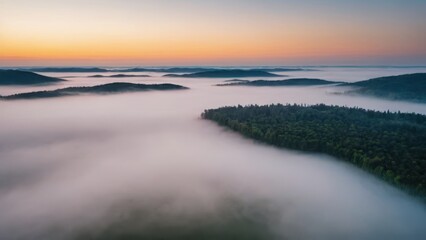 Fototapeta premium A breathtaking aerial view of islands covered in dense forest, surrounded by thick layers of fog floating over a serene lake. The mist blankets the valleys between the hills, creating a surreal, other