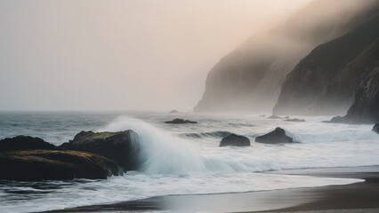 Fototapeta premium Fog-covered cliffs loom in the background as ocean waves crash over the dark rocks along the shoreline. The soft, misty light and quiet sea create a sense of peaceful isolation.