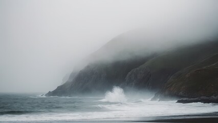 Naklejka premium Fog-covered cliffs loom in the background as ocean waves crash over the dark rocks along the shoreline. The soft, misty light and quiet sea create a sense of peaceful isolation.