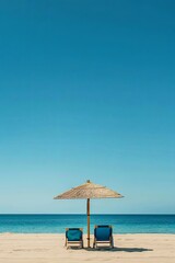 Two blue beach chairs under a straw umbrella on a sandy beach with a clear blue sky and ocean in the background.