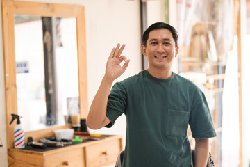 Obraz premium A man is confidently giving an ok sign while sitting in a barber shop, showcasing his satisfaction with the service he is receiving