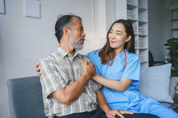 Fototapeta premium Young female doctor is comforting an elderly male patient while holding his hand at his home