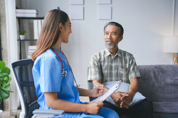 Obraz premium Young female doctor is holding a clipboard and talking to a senior male patient sitting on a sofa in the living room