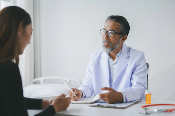 Fototapeta premium Senior male doctor is taking notes while explaining a diagnosis to his female patient