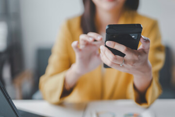 Businesswoman is using a smartphone while sitting at her desk in an office, with a laptop computer in the foreground