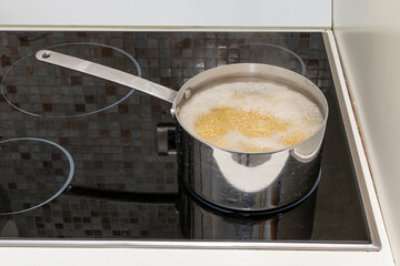 Pasta cooking inside metal pot on glass stove panel inside kitchen interior