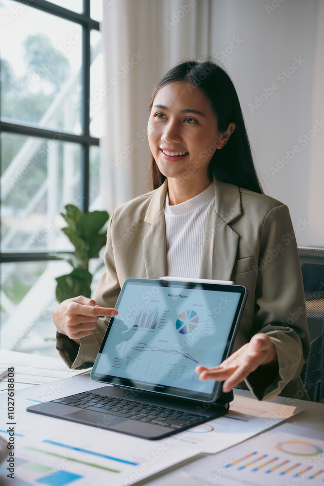 Poster smiling asian businesswoman pointing at charts and graphs on a tablet while making a business presen
