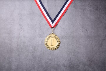 Golden medal with striped ribbon on grey background, top view