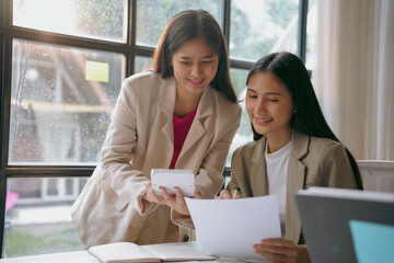 Two young businesswomen are discussing over financial documents and using calculator while working together in office