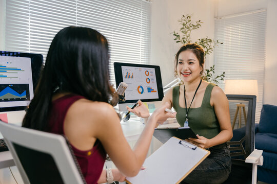 Two asian businesswomen discussing marketing data while recording a podcast in a modern office. Working together on strategies for growth, surrounded by technology