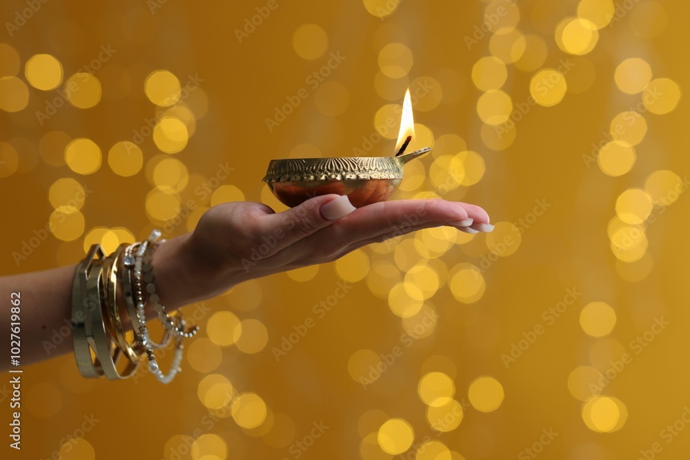 Sticker Diwali celebration. Woman holding lit diya lamp on color background with blurred lights, closeup