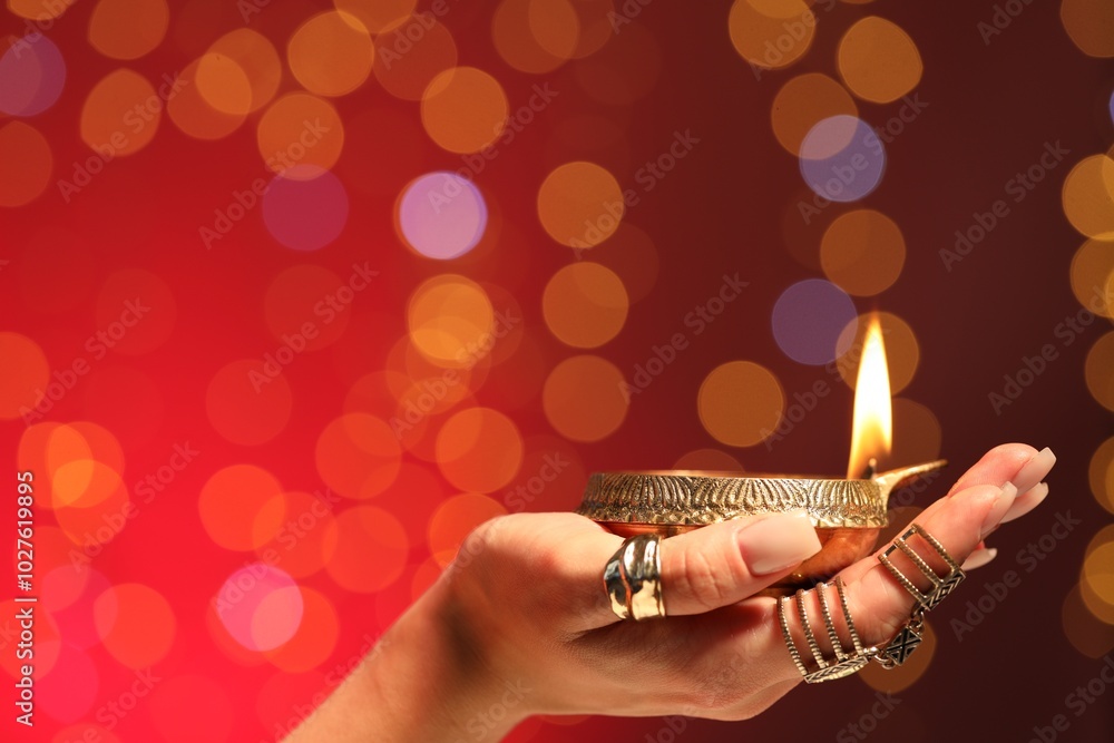 Canvas Prints Diwali celebration. Woman holding lit diya lamp on red background with blurred lights, closeup. Space for text